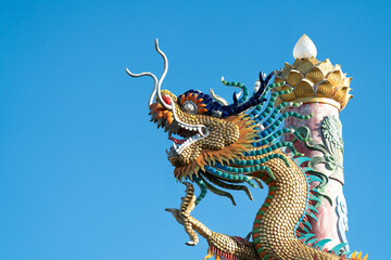 Ornate Chinese dragon sculpture with golden scales and vibrant mane against a clear blue sky. Traditional architectural element from a temple, showcasing intricate craftsmanship and heritage.