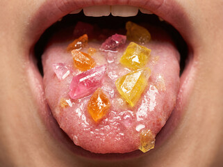 Colorful hard candy shards on tongue, extreme macro close-up of mouth