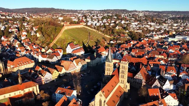A wide panorama of Esslingen shows historic urban architecture with church towers, dense rooftops, a green hillside, and trees in clear daylight. Ideal for travel, tourism, lifestyle, editorial.
