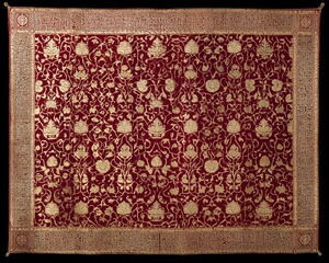 Traditional Islamic textile pattern with intricate floral and geometric motifs woven into rich fabric in gold, burgundy, and blue hues