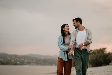 Happy couple walking on riverbank at sunset, enjoying romantic moment