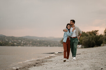 Happy couple walking on the beach at sunset, embracing and smiling
