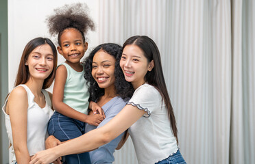 Obraz premium Happy diverse multiethnic group of women hugging with little african american girl at home, asian and black friends smiling with child, family, adoption, unity and friendship concept