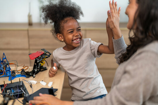 Happy african american girl high five with mother after building robot at home, Child learning STEM coding and engineering, education, science technology, family teamwork and success concept