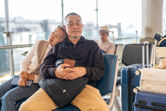 Tired senior asian couple sleeping on airport chairs while waiting for flight, Elderly husband and wife napping with luggage, retirement travel, flight delay, jet lag and insurance concept