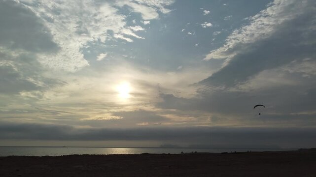 sunset over ocean with paraglider silhouette drifting across dramatic cloudscape, golden light