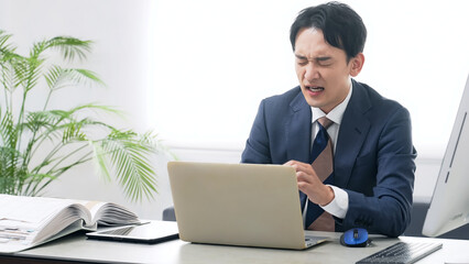 オフィスでPCを使って作業しながら悩む男性ビジネスパーソン