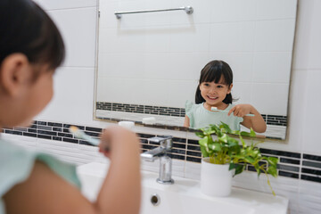 girl child brushing teeth at reflection in mirror in bathroom