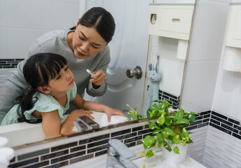 stubborn child girl refusing to brush her teeth in the bathroom. mother is trying to encourage her unhappy daughter during the morning routine, while child looks grumpy and resistant.
