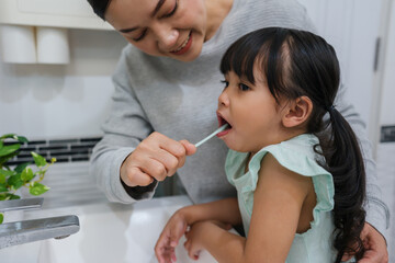mother teaching girl child to brushing teeth in bathroom