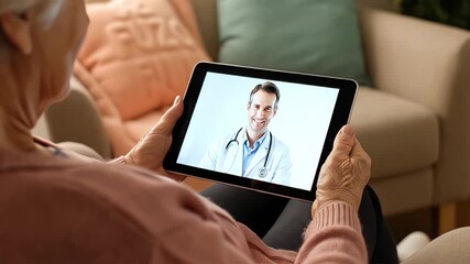 Over the shoulder view of an elderly woman engaging in a telemedicine video consultation with a male doctor on a digital tablet - Powered by Adobe