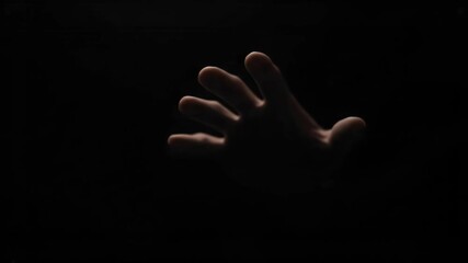 Dramatic hand reaching out from total darkness seeking help or grasping in mysterious shadowy void