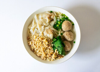 A bowl of Chinese-style chicken noodles with beef balls and dumplings. Delicious Asian comfort food featuring minced meat topping, isolated on white.