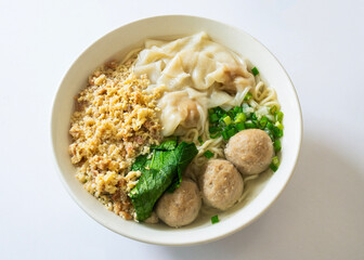 A bowl of Chinese-style chicken noodles with beef balls and dumplings. Delicious Asian comfort food featuring minced meat topping, isolated on white.
