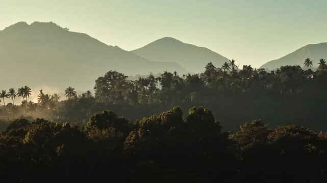 Lombok Senaru mountains landscape creating a layered hazy silhouette, light mist rises from tropical jungle canopy trees forest at the magic hour sunset. Natural background. Aerial flight footage