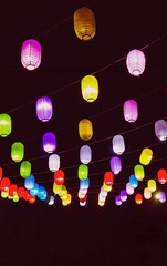 Decorative colorful paper lanterns hanging and glowing at night in urban street.