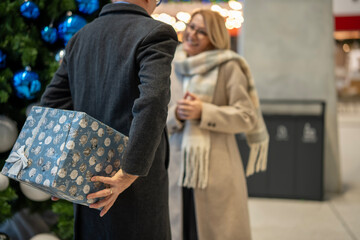 Man surprising woman with wrapped gift behind back