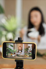 A young woman films herself applying a skincare product while surrounded by natural ingredients and...