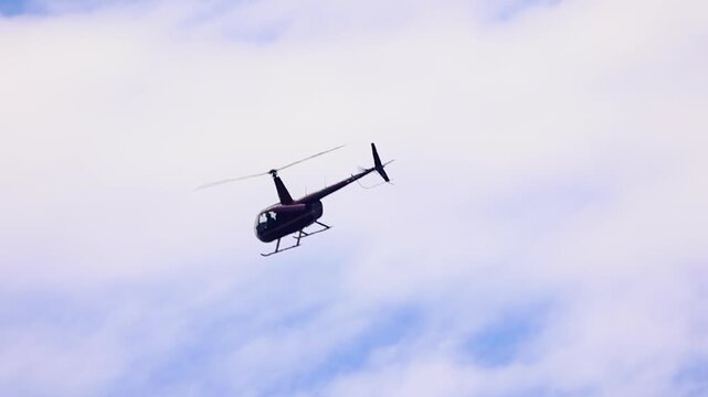 Slow motion R66 helicopter flies through cloudy sky, medium shot