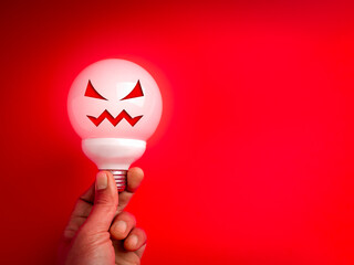 Creative concept of a bad idea with spooky face light bulb on red background with copy space, representing failure, danger, scary thinking, wrong decision, and Halloween-style innovation warning.