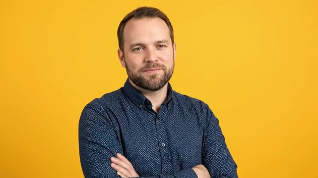 A confident and friendly man with a well-groomed beard smiles warmly directly at the camera, his arms comfortably crossed. He wears a stylish dark blue patterned collared shirt, projecting an approach