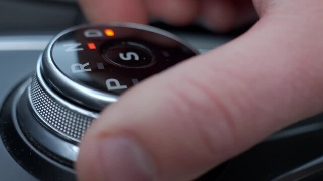 Close-up of hand turning gear shift knob in modern car interior. Driver switches transmission in drive mode on automatic gearbox