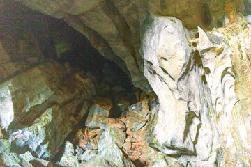 Irregular limestone formations and rugged boulders define a shadowy passage inside Phu Kham Cave in Laos. Subtle mineral stains and carved surfaces are illuminated by artificial light, emphasizing the © Florent