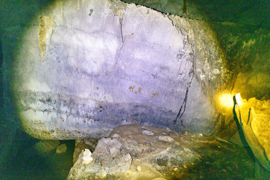 A rugged limestone wall inside Phu Kham Cave in Laos displays faded handprints and painted symbols under artificial light. The scene highlights textured rock surfaces, subtle mineral layers, and the