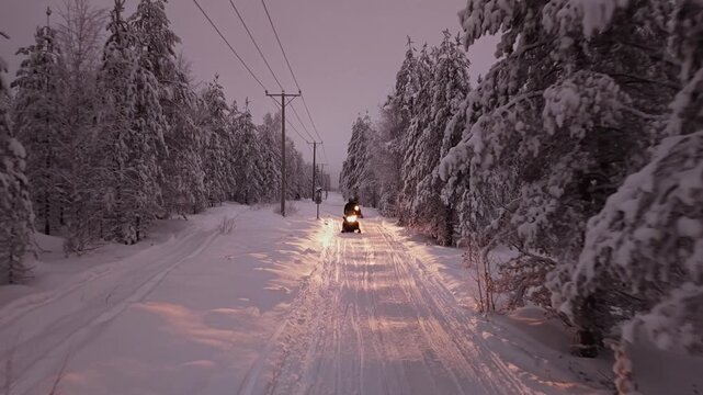 Winter snowmobile adventure through pine forest trails, Lapland, Snow covererd landscape, Arctic Circle, Aerial tracking shot