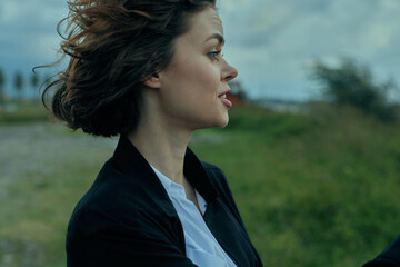 Woman in blazer outdoors, wind in hair, profile facing the horizon, conveying professional focus,...