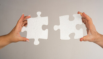 Two hands trying to connect puzzle piece on gray background. Teamwork concept. Closeup hand of...
