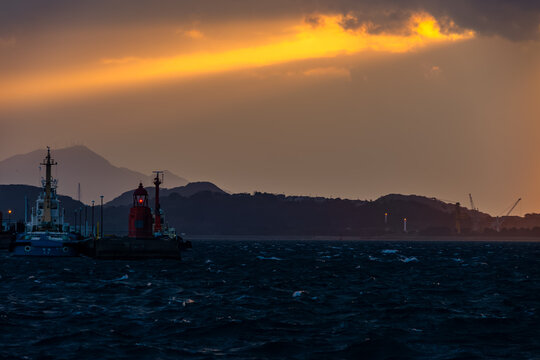 夕暮れの関門海峡の青い荒ぶる波と雲間から刺す一条の黄金の光と赤い灯台の灯り 20210128-1