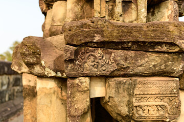 Close-up of intricately carved sandstone blocks at Bakong temple in Cambodia, showing weathered patterns and ancient motifs under warm natural light. The textured stone surfaces highlight the © Florent