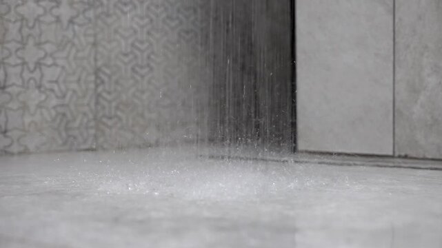 Strong stream of water from a shower head falling and splashing onto a contemporary gray tiled floor, creating sparkling droplets and a relaxing, refreshing atmosphere in a modern bathroom