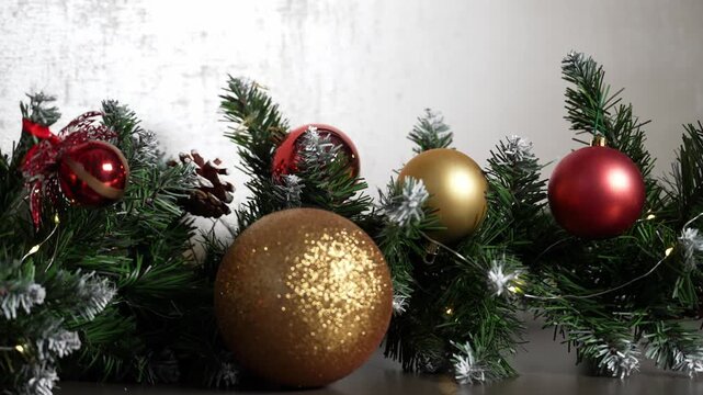 A beautiful display of Christmas ornaments resting on a dark surface. Ornaments of gold and red shimmer amongst the vivid, snowy-tipped needles of an evergreen branch.