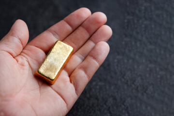 Human hand holding gold bar symbolizing wealth, investment, financial security, inflation hedge, and precious metal value.