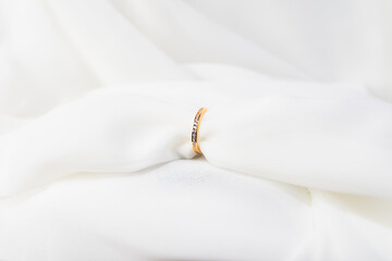 Naklejka premium A gold band is placed on a white cloth, which is likely a wedding band. The band is positioned in the center of the cloth, and it is a simple, elegant piece of jewelry.
