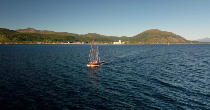 Aerial drone view of a traditional sailboat cruising in the Lofoten Islands. The scenic coastline and mountains are visible in the background, Norway