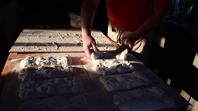 Close-up of baker shaping and spreading focaccia dough by hand on wooden board