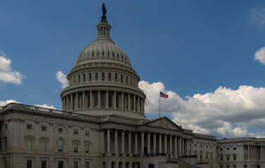 Obraz premium Capitol dome against blue sky. Washington DC federal landmark. United States Capitol architecture. Congress building in the capital. American government. Flag waving at Capitol Hill.