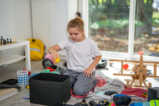 Child cleaning messy playroom at home. Kid organizing scattered toys on the floor. Kid helping tidy up children messy room. Boy cleaning untidy playroom interior. Kid picking up toys in messy room.