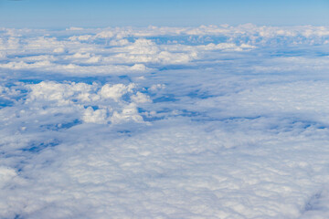 Naklejka premium Aerial view of soft white clouds and blue sky seen from airplane window. Peaceful travel and aviation background.