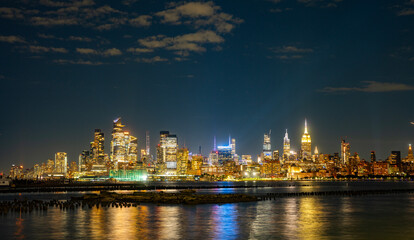 Naklejka premium Iconic city view of New York in night. NY night towers above the Hudson. NYC night skyscrapers against the sky. Famous New York panorama. Classic New York cityscape panoramic view.