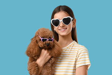Teenage girl with cute Toy Poodle dog in sunglasses on blue background