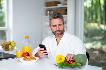 Fototapeta premium Hispanic Man eats breakfast in the kitchen on a morning. A man enjoys fresh food at the kitchen table. A man eats cereal and fruit in the kitchen. Guy enjoys eggs and vegetables at the modern kitchen.