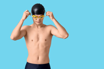 Young male swimmer with goggles on blue background
