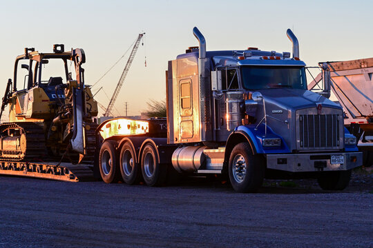 Kenworth semi-truck hauling an excavator loader on a trailer at a construction yard, representing heavy equipment transport, site logistics, and industrial operations