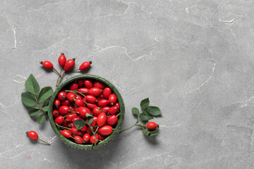 Bowl with fresh rose hip berries and leaves on grey background