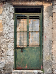 old rusty metal green door on old stone wall exterior on abandoned house