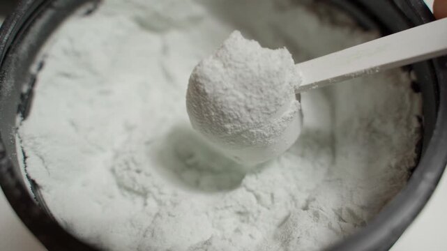 Taking a scoop of creatine from a jar, close-up